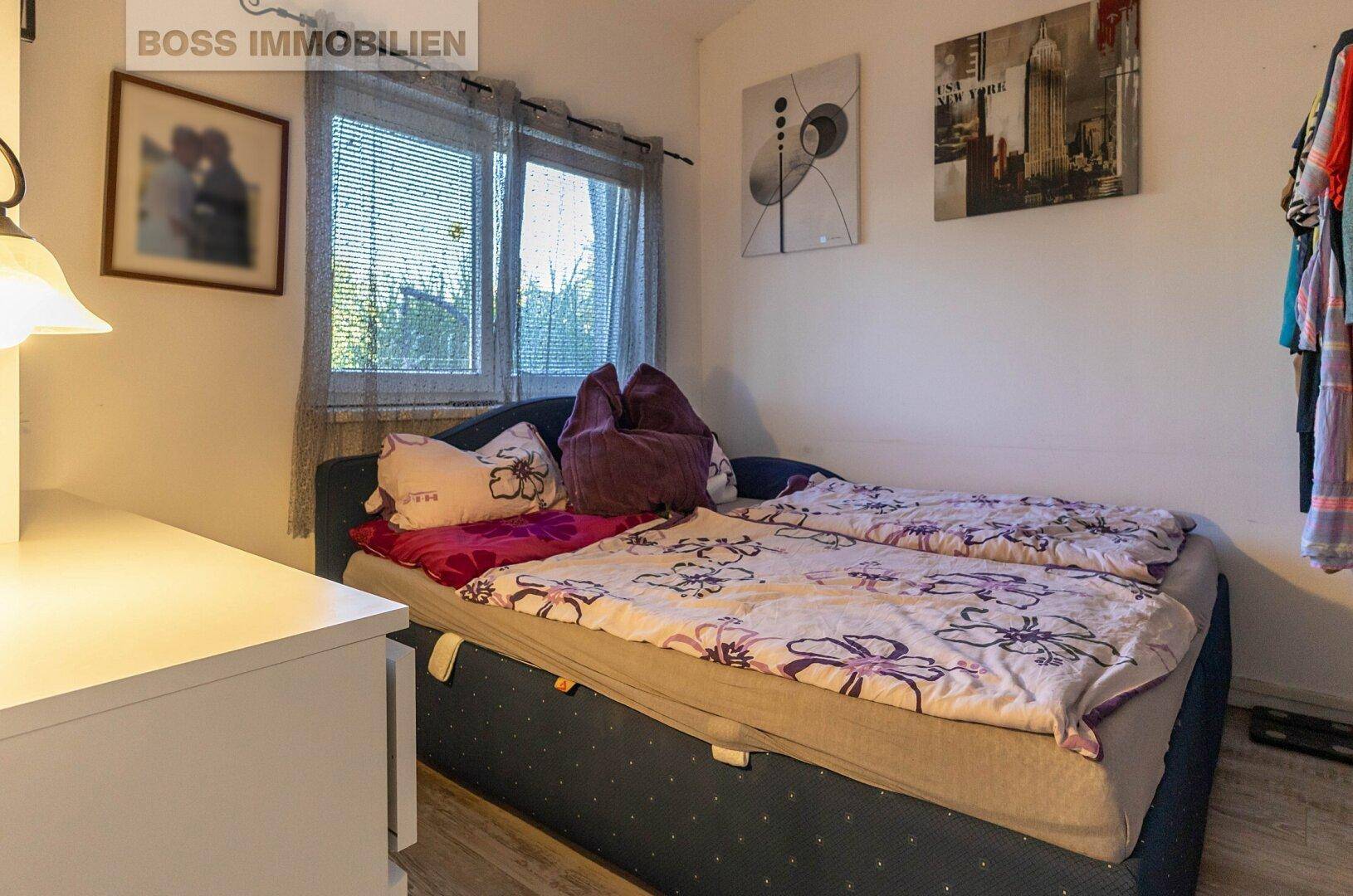 Schlafzimmer mit Einzelbett, Fenster mit Jalousien und einfacher Einrichtung.