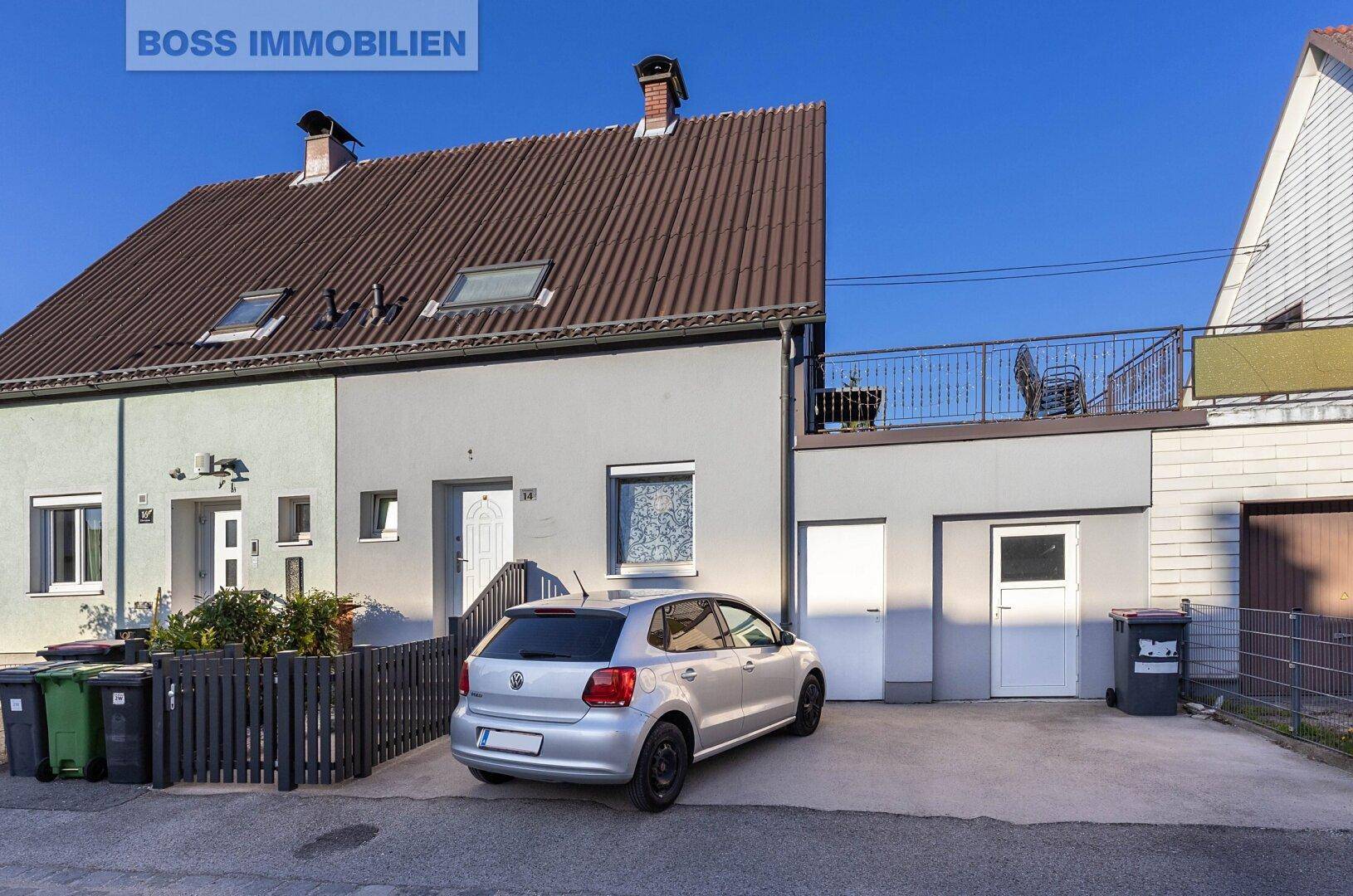 Außenansicht eines Reihenhauses mit geparktem Auto und Dachfenstern unter blauem Himmel.
