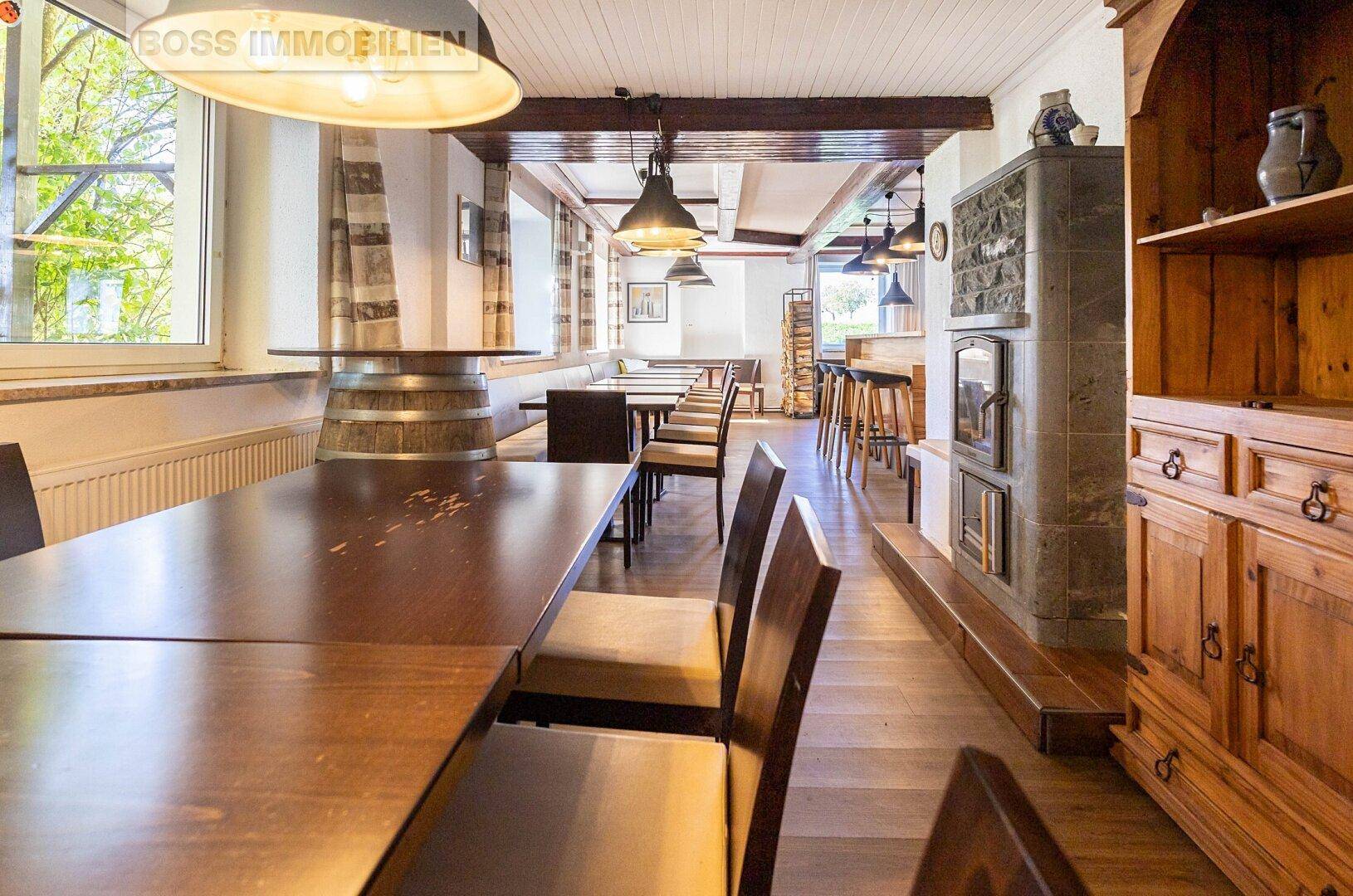 Langer Restaurantbereich mit Holztischen, Stühlen, einem Kamin und einem traditionellen Holzschrank.