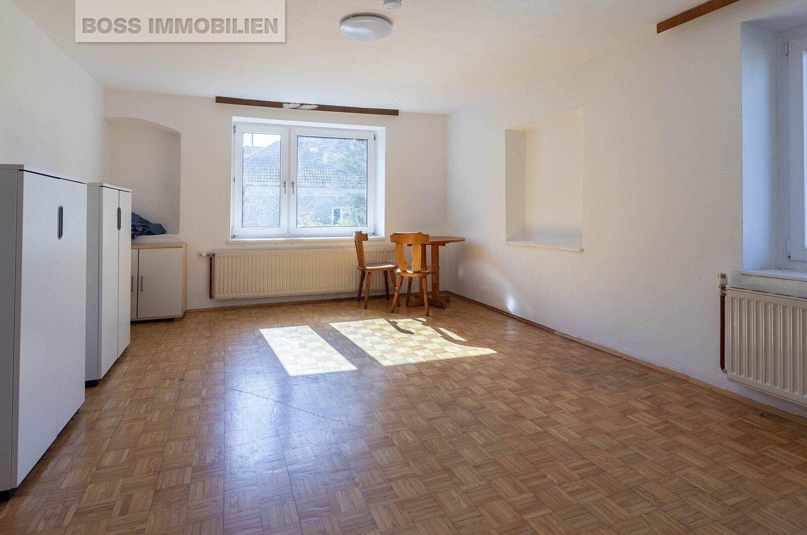 Geräumiges Schlafzimmer mit Parkettboden, Fenster und einfacher Möblierung, gut beleuchtet.