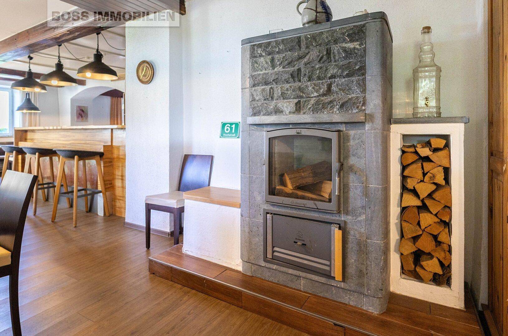 Detailansicht eines Steinkamins mit sichtbarem Brennholz in einem Gastraum mit Bar im Hintergrund.
