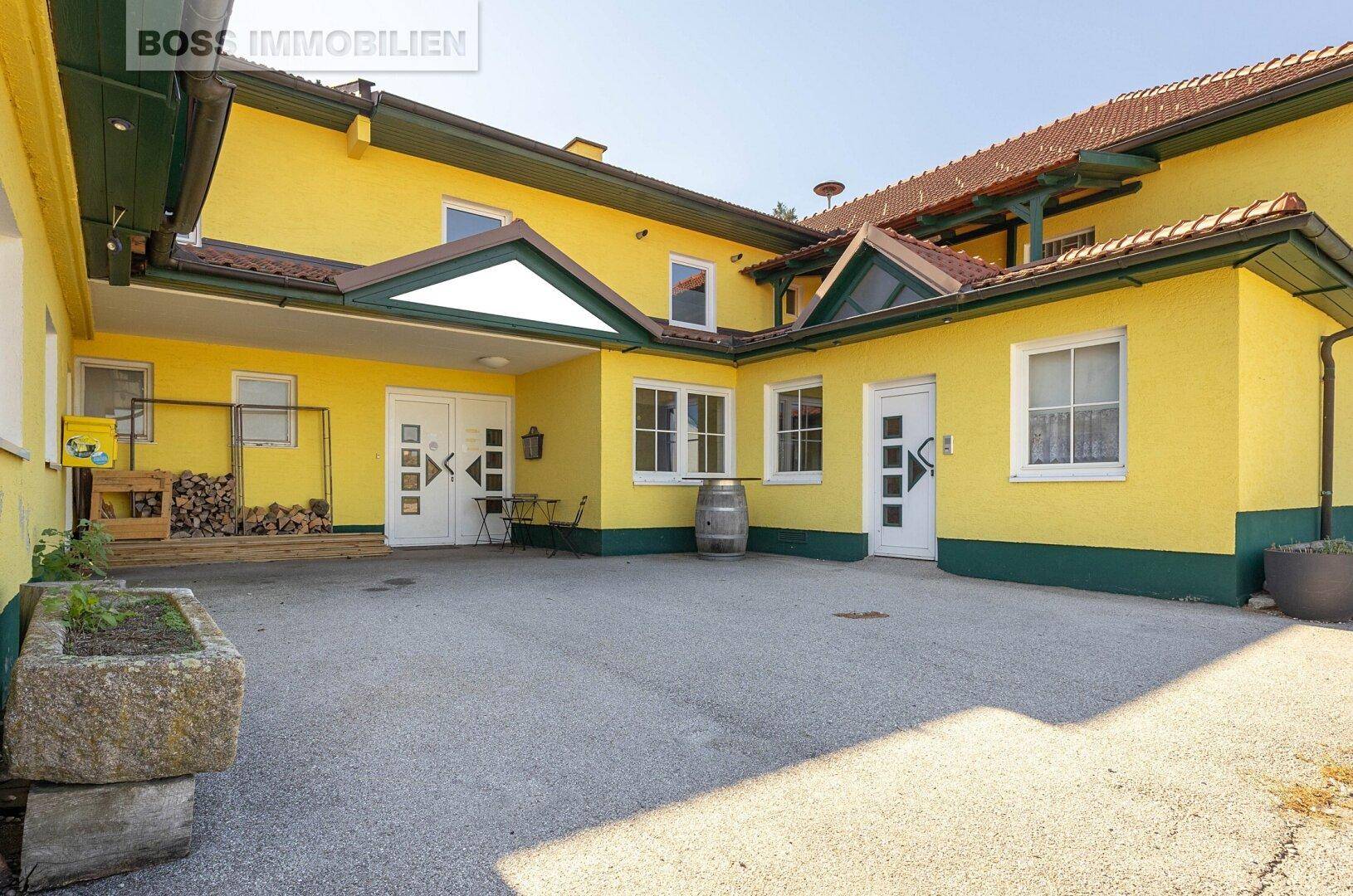 Gelbes Gebäude mit grünen Akzenten und einem gepflasterten Hofbereich, der als Eingang dient.