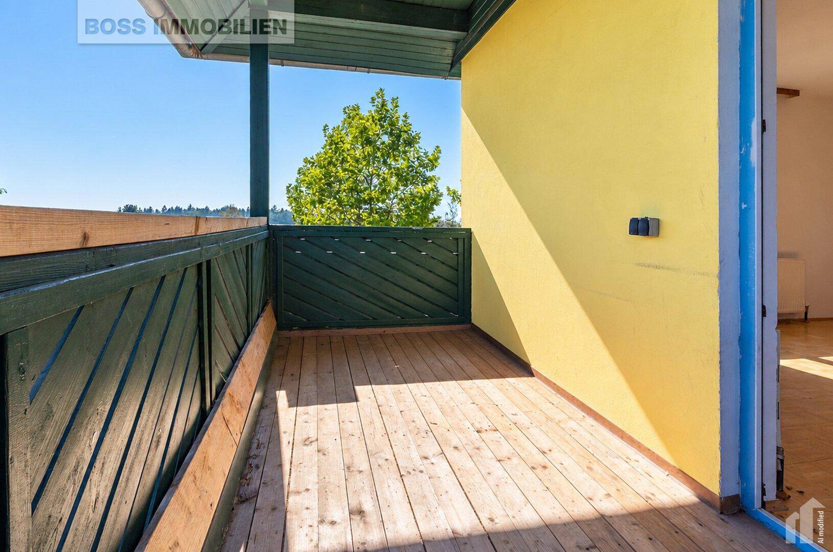 Sonniger Balkon mit Holzboden und grünen Geländern, bietet einen Blick ins Grüne.