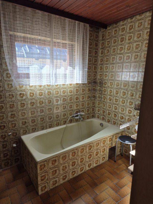 Badezimmer mit Badewanne und gemusterten Fliesen an Wänden und Boden, mit Fenster.