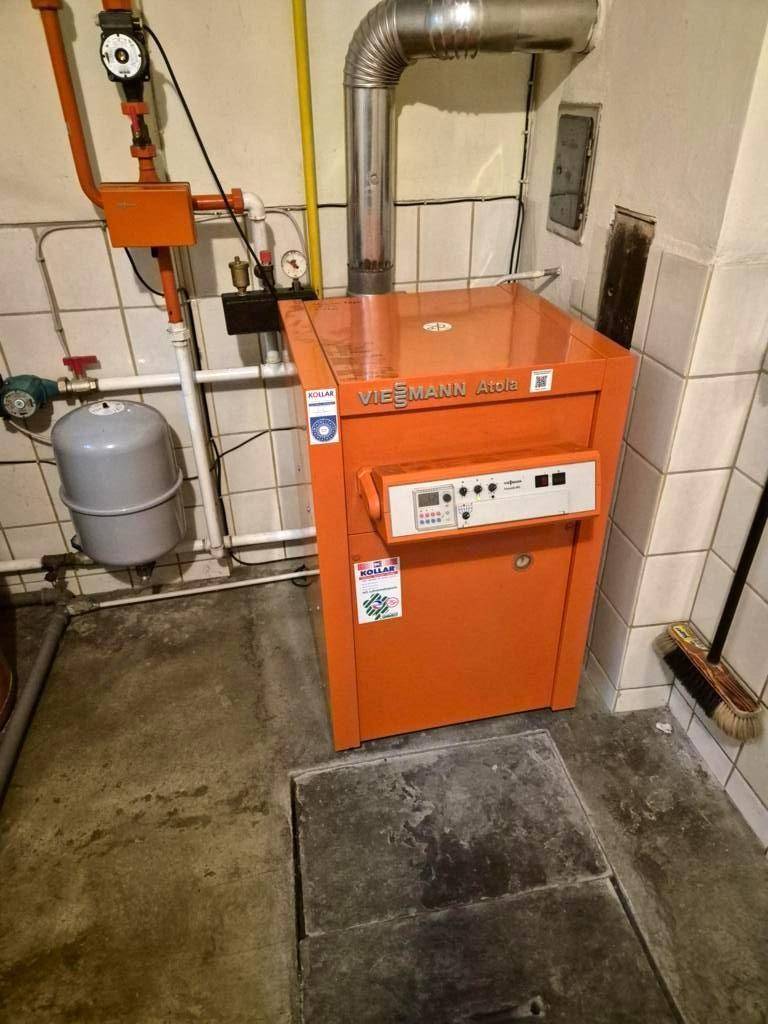 Heizungsraum mit einem orangefarbenen Viessmann Heizkessel und gefliesten Wänden.