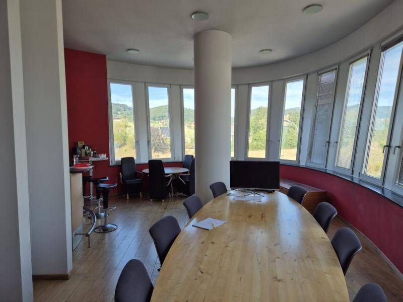 Runder Konferenzraum mit Holztisch, vielen Fenstern und weitem Blick auf die Landschaft.