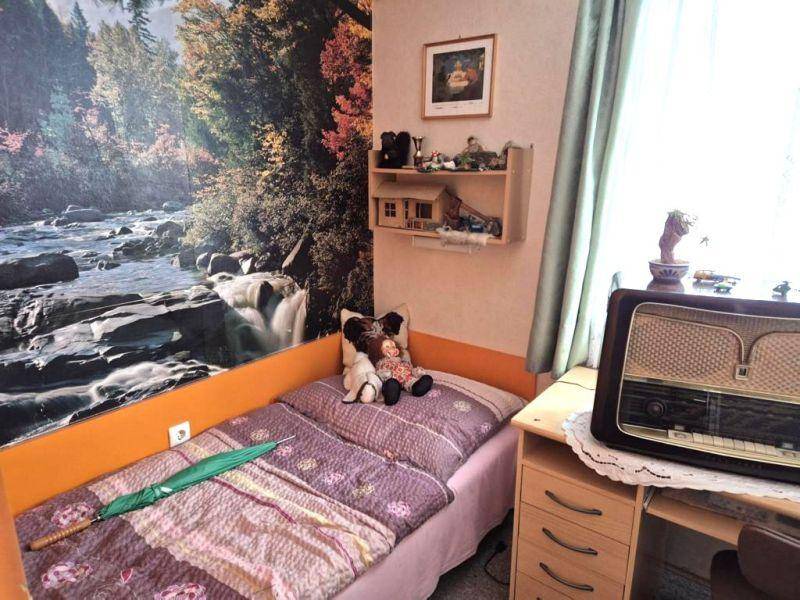 Gemütliches Schlafzimmer mit Einzelbett, farbiger Wandtapete und Vintage-Radio auf dem Nachttisch.