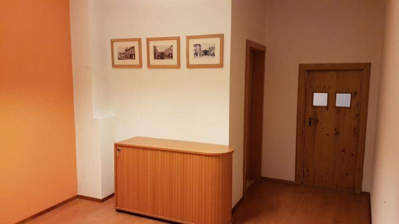 Flur oder Büroraum mit hellem Boden, einer orangefarbenen Akzentwand und Holzmöbeln.