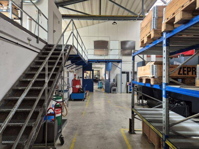 Große Lagerhalle mit hohen Regalen, Metalltreppe und industrieller Ausstattung.