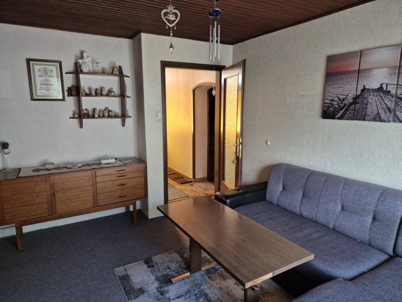 Wohnzimmer mit Sofa, Holzmöbeln und Blick auf den Flur, typisch für ältere Einrichtung.