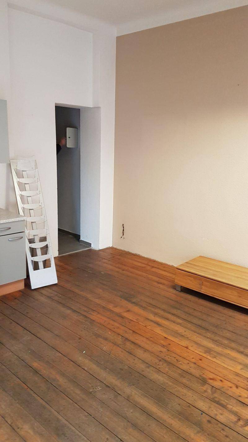 Raum mit dunklem Holzplankenboden und heller Wandfarbe, teilweise mit Küchenzeile ausgestattet.