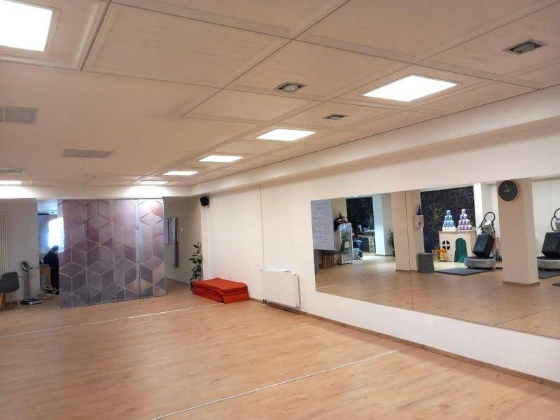 Geräumiger Fitnessraum mit Spiegelfront, Holzboden und einem abgetrennten Bereich mit Glaswand.