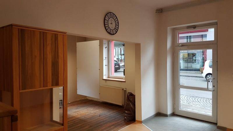 Eingangsbereich mit Glastür, Fenster und einem Holzschrank, Bodenübergänge von Holz zu Fliesen.