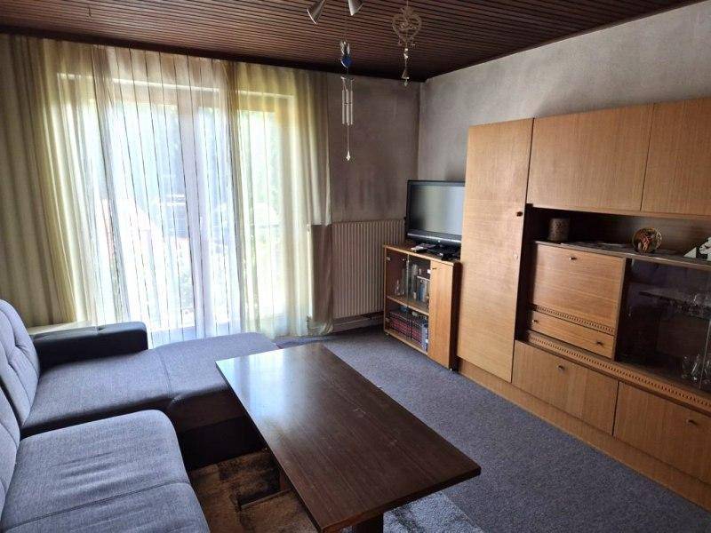 Gemütliches Wohnzimmer mit Sofa, Couchtisch und Zugang zum Balkon durch große Fenster.