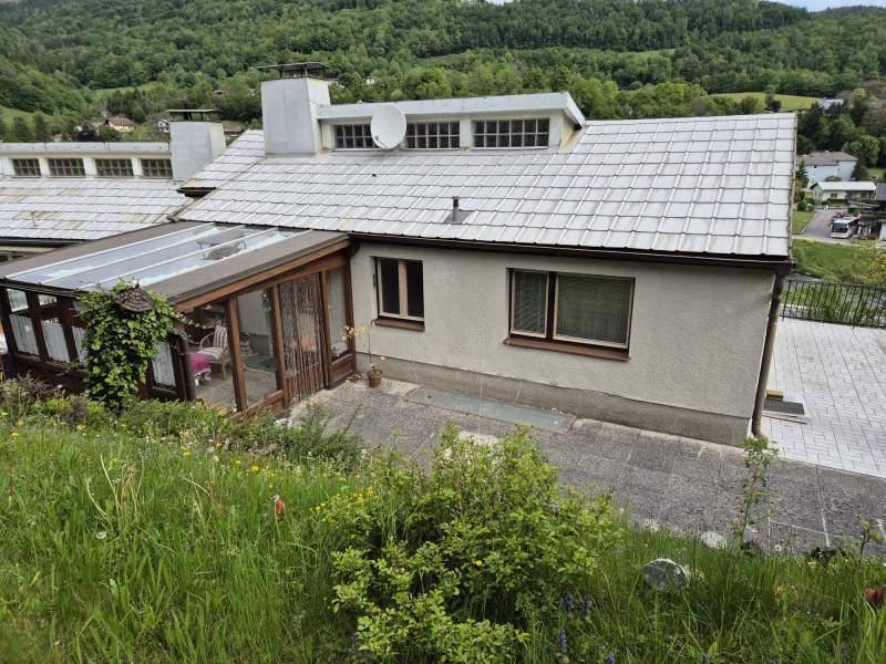 Rückseite des Hauses mit angebautem Wintergarten und gepflasterter Terrasse.