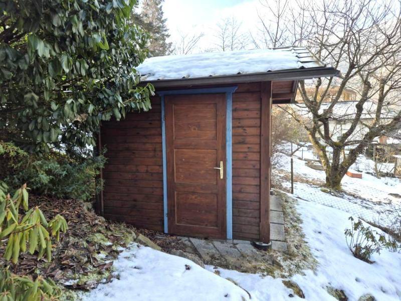 Kleiner Holzschuppen im Garten, umgeben von Schnee und Bäumen, mit blauen Akzenten.