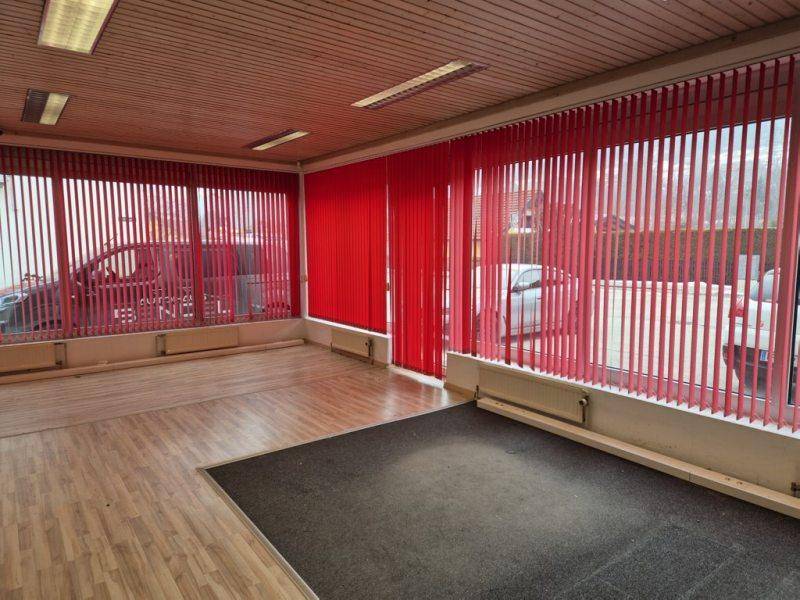 Heller Gewerberaum mit Holzdecke, Laminatboden und auffälligen roten Vertikaljalousien an den Fenstern.