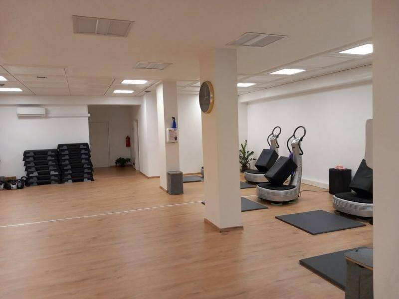 Heller Fitnessbereich mit Holzboden, Säulen und modernen Vibrationsplatten für das Training.