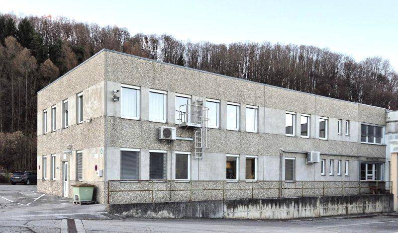 Rückansicht des Geschäftsgebäudes mit Betonfassade, Klimaanlagen und Blick auf bewaldete Hügel.