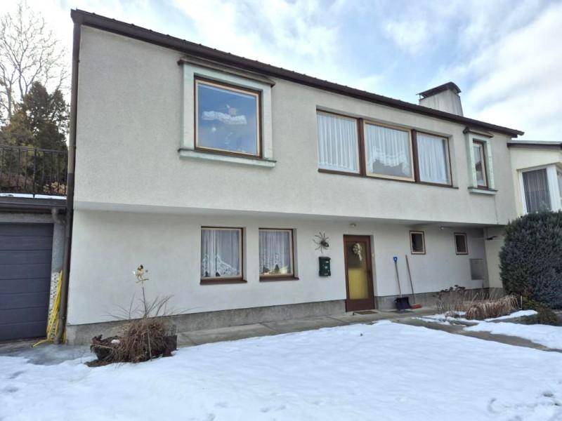 Gesamtansicht des Hauses von vorne mit verschneitem Garten und Blick auf die bewaldeten Hügel.