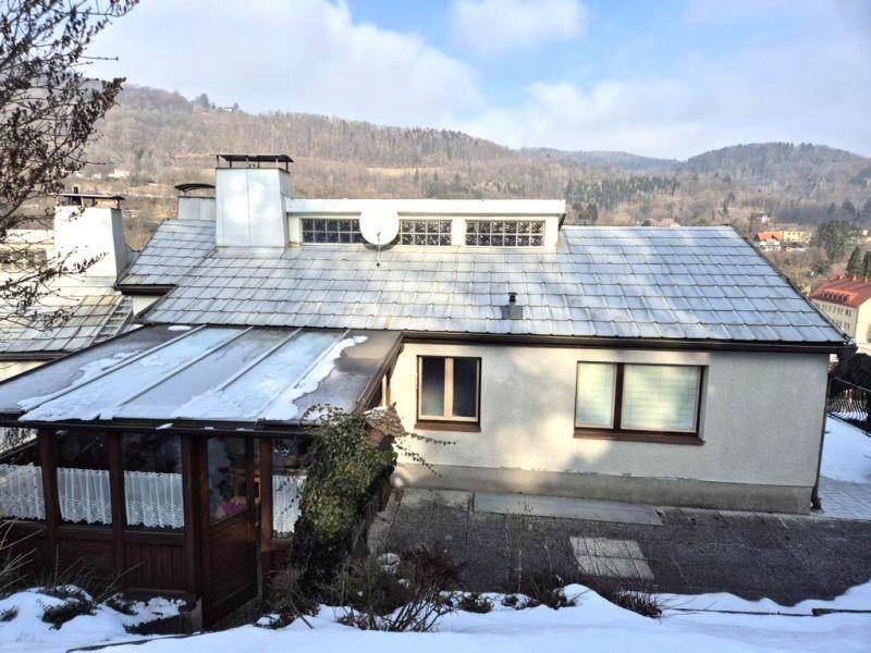 Rückansicht des Hauses mit Dach, Wintergarten und verschneiter Landschaft im Hintergrund.