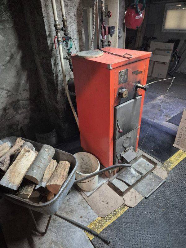 Heizraum im Keller mit einem Holzofen und Brennholz, bereit zur Nutzung.