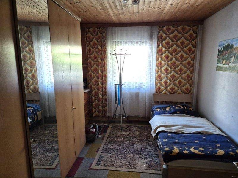 Kleines Schlafzimmer mit Einzelbett, Holzdecke und gemusterten Vorhängen am Fenster.