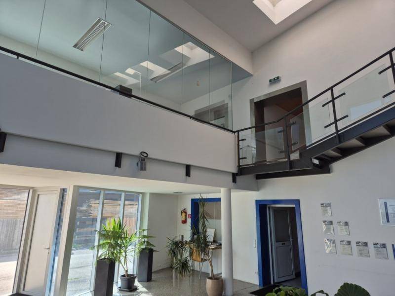 Heller Empfangsbereich mit hoher Decke, Galerie und Treppe mit Glasgeländer.