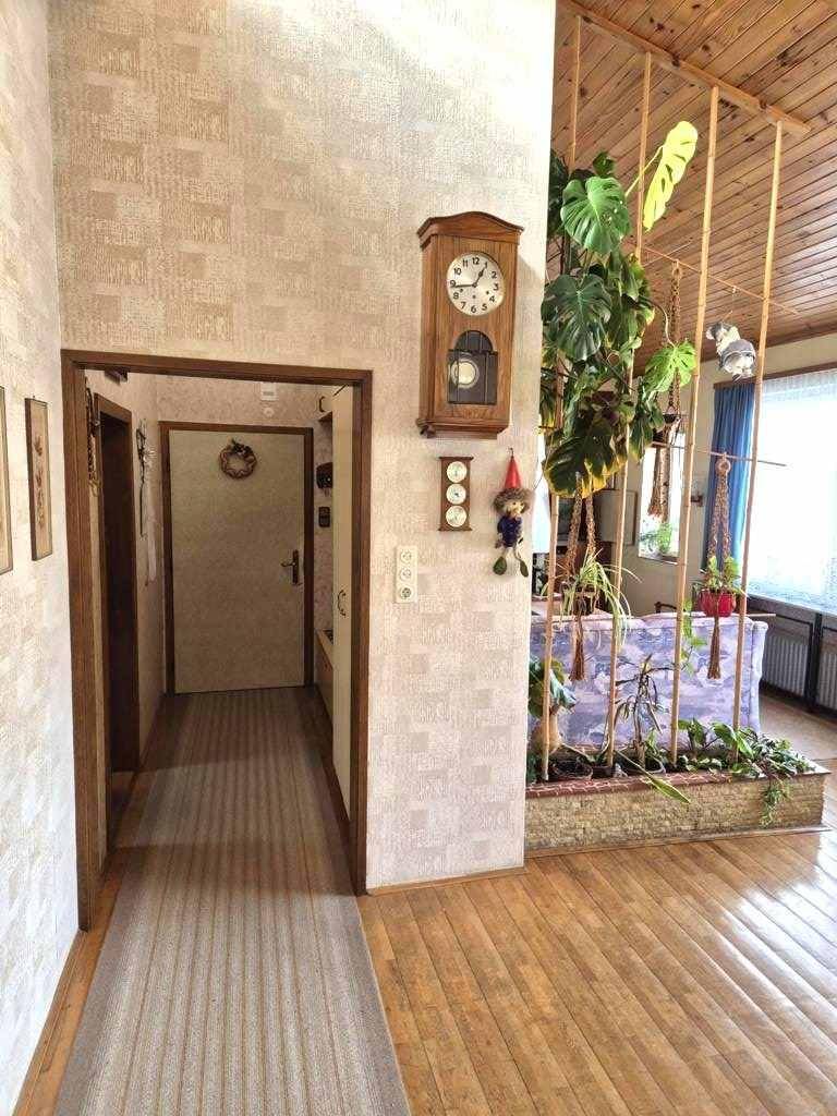 Flur mit Holzboden, strukturierten Tapeten und einer Wanduhr, die zum Wohnbereich führt.