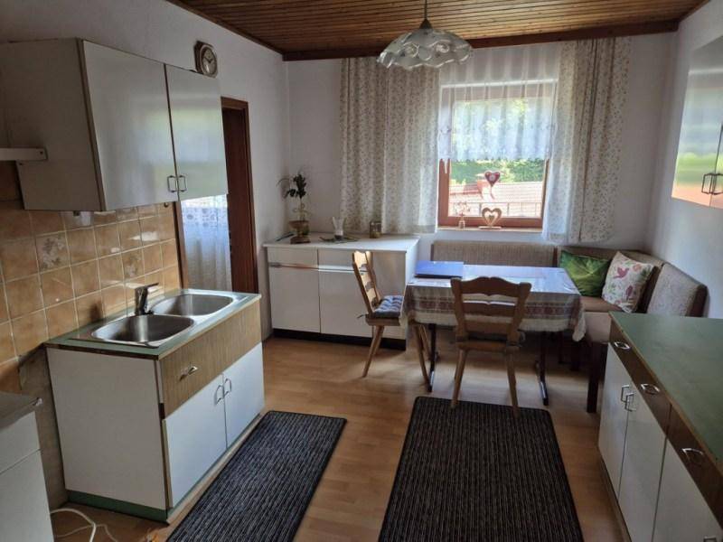 Einfache Küche mit Essbereich, Holzdecke und Fenster, ausgestattet mit älteren Möbeln.