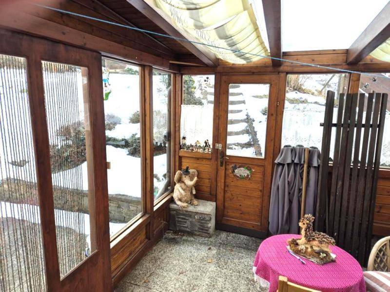 Gemütlicher Wintergarten mit Holzrahmen, Glaswänden und Blick auf die verschneite Umgebung.