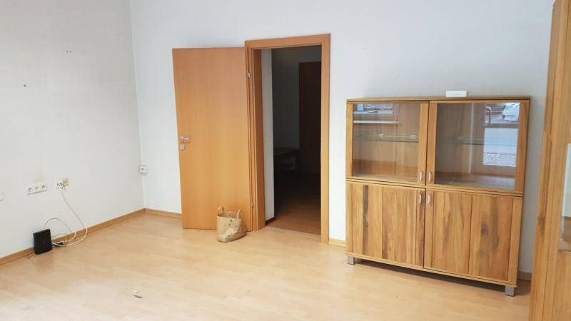 Leerer Raum mit hellem Laminatboden, weißen Wänden und einem Holzschrank, bereit zur Einrichtung.