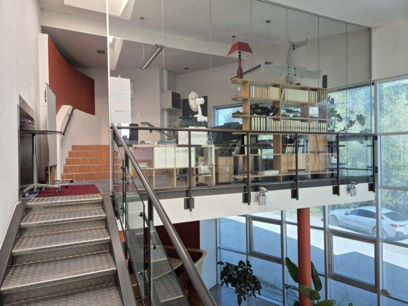 Treppenhaus führt zu einem offenen Bürobereich mit Glasgeländer und Blick nach draußen.