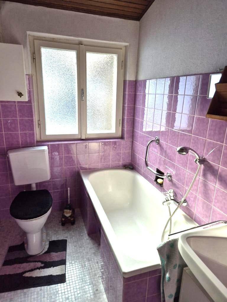 Badezimmer mit lila Fliesen, Badewanne, Toilette und Fenster für Tageslicht.