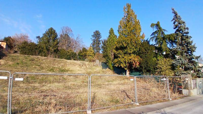 Unbebautes Grundstück mit Bauzaun und üppigem Baumbestand unter klarem Himmel.