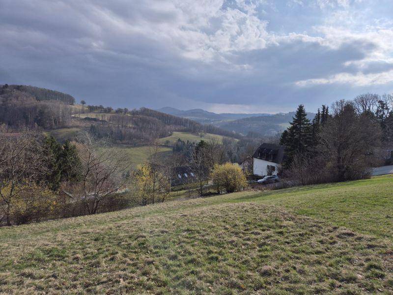 Weitläufiges Wiesengrundstück mit Blick auf ein Tal, bewaldete Hügel und ein Haus am Hang.