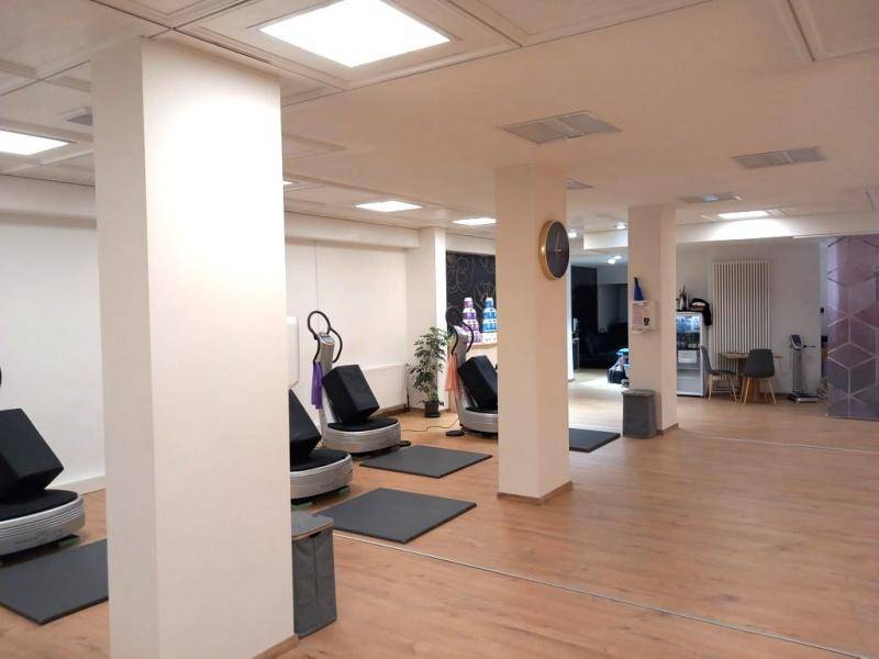 Heller Trainingsbereich mit Holzboden, Säulen und verschiedenen Fitnessgeräten in einem modernen Ambiente.
