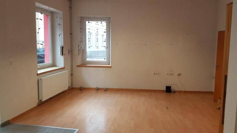 Heller Raum mit Laminatboden, weißen Wänden und zwei Fenstern mit Blick auf die Straße.