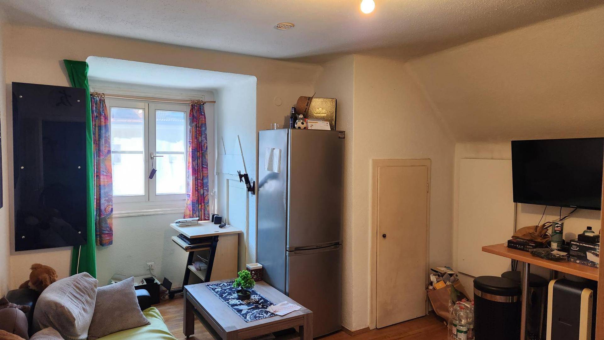 Gemütliches Dachgeschosszimmer mit Dachschrägen, Fenster und Kühlschrank.