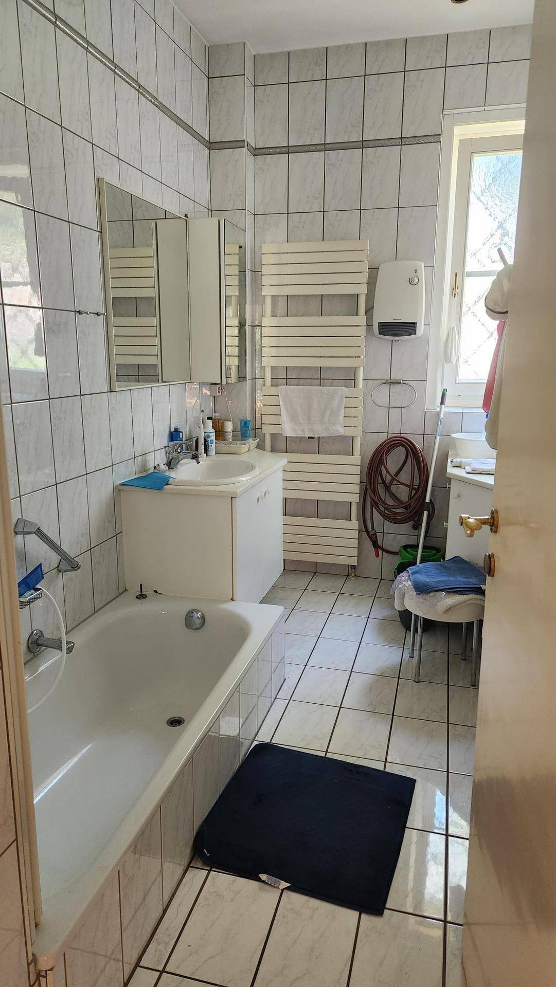 Badezimmer mit Badewanne, weißen Fliesen, Einzelwaschbecken und Fenster.