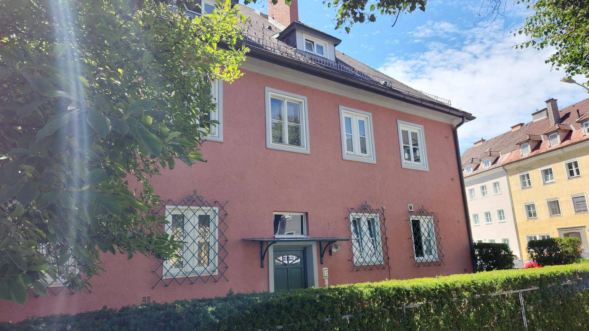 Vorderansicht des Gebäudes mit roter Fassade, weißen Fenstern und einem grünen Eingangsbereich.