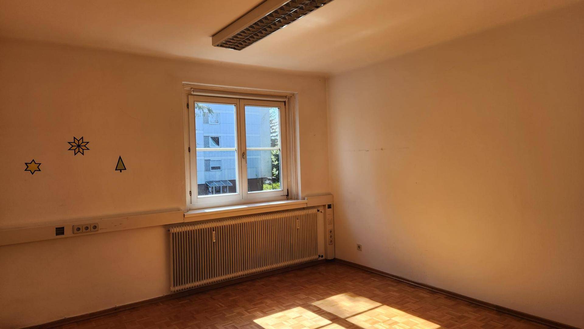 Heller, leerer Büroraum mit Holzboden und einem Fenster, das den Blick nach draußen freigibt.