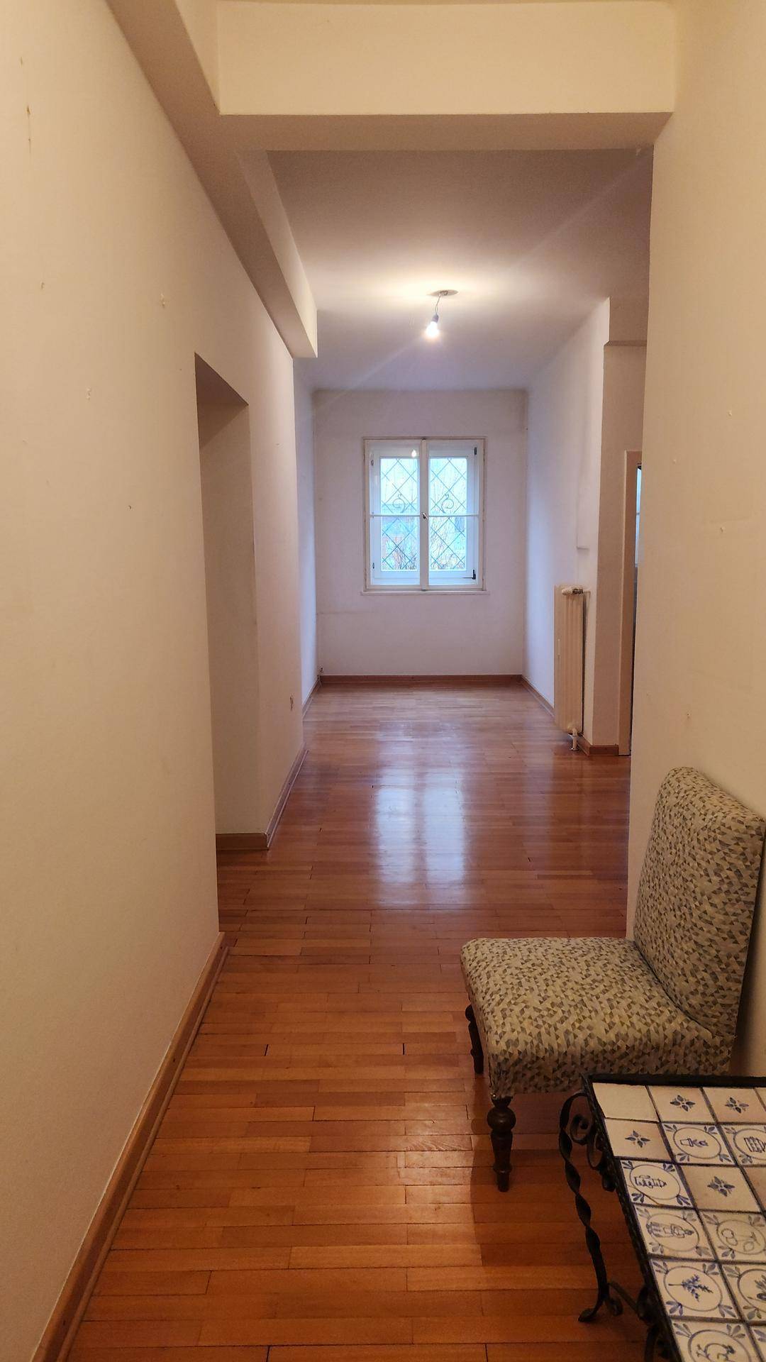 Langer Flur mit Holzplankenboden, hellen Wänden und einem Fenster am Ende des Ganges.