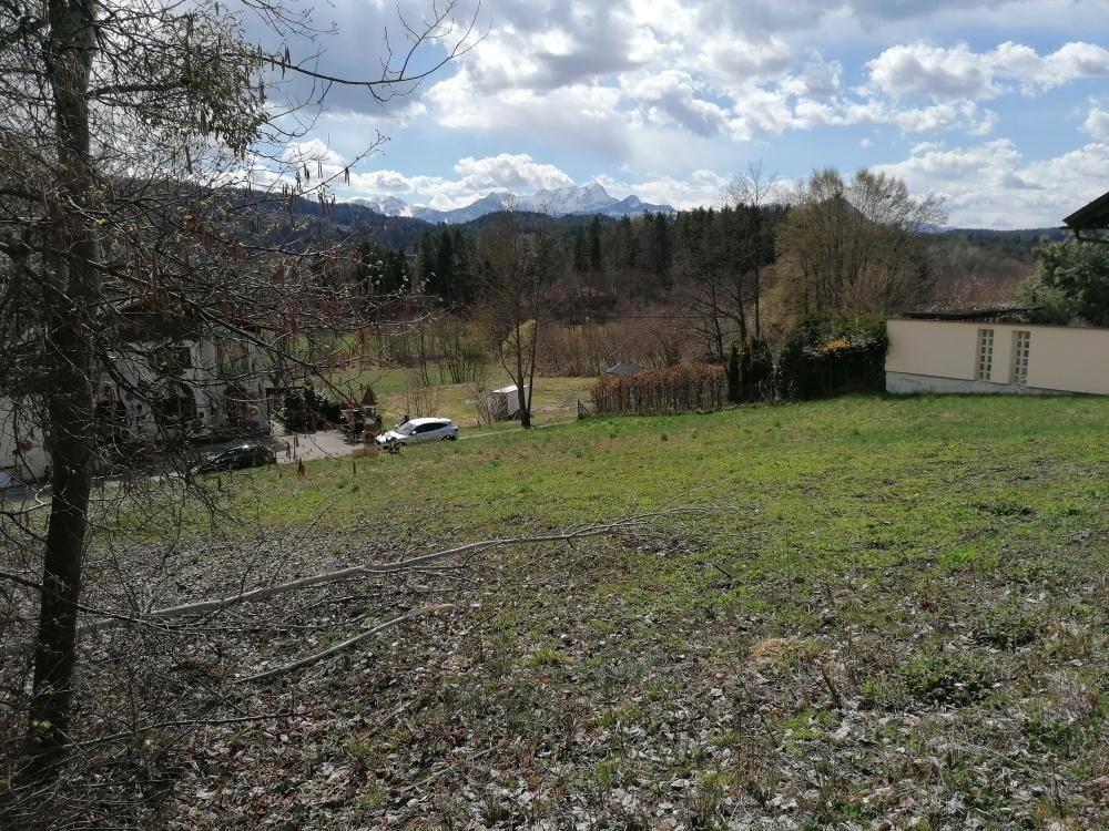 Grünes Grundstück mit weitem Blick auf eine Bergkette, Bäume und einige Gebäude in der Landschaft.