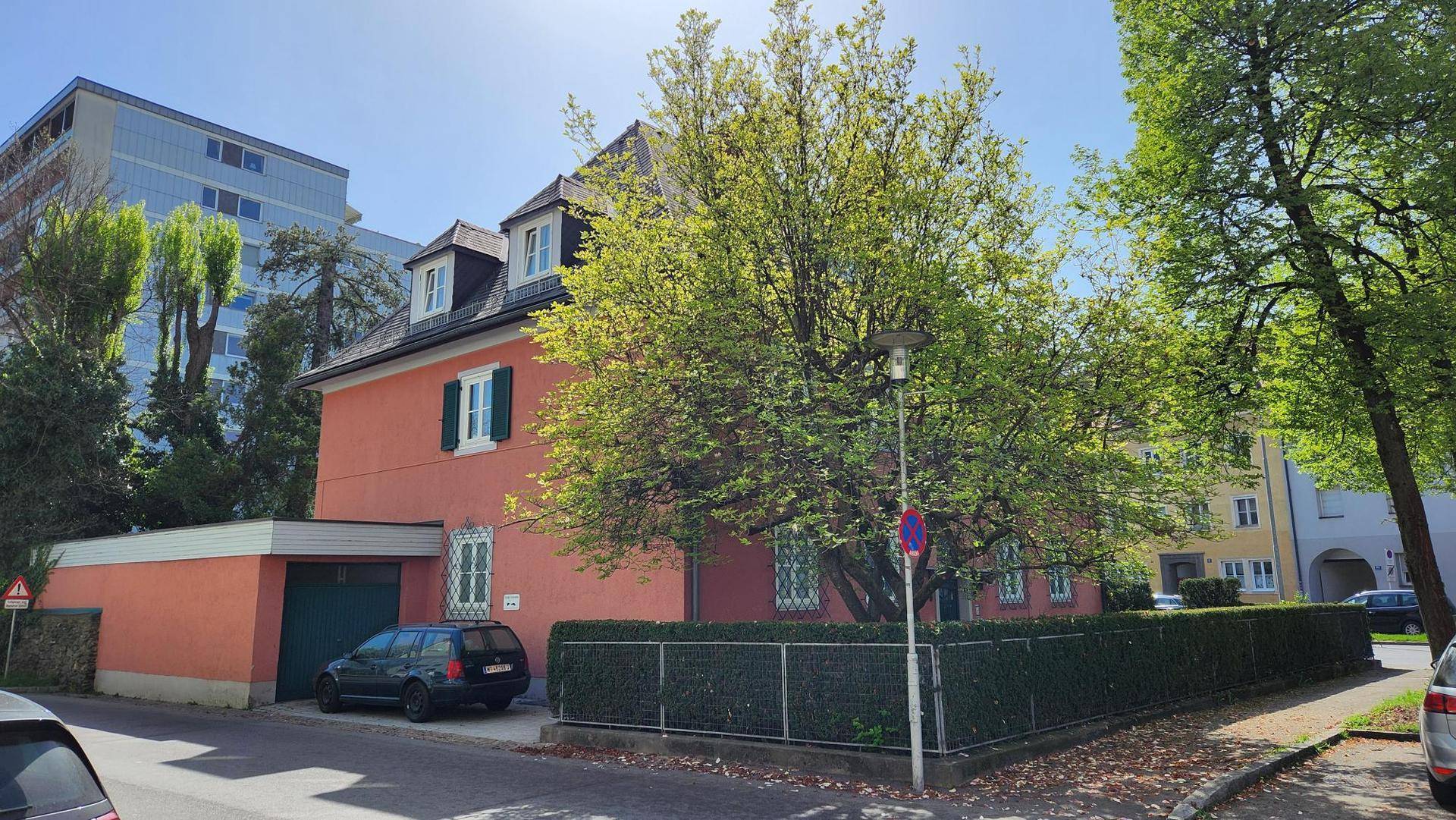 Ansicht des roten Gebäudes von der Straße mit Garage, Hecke und umliegenden Bäumen.