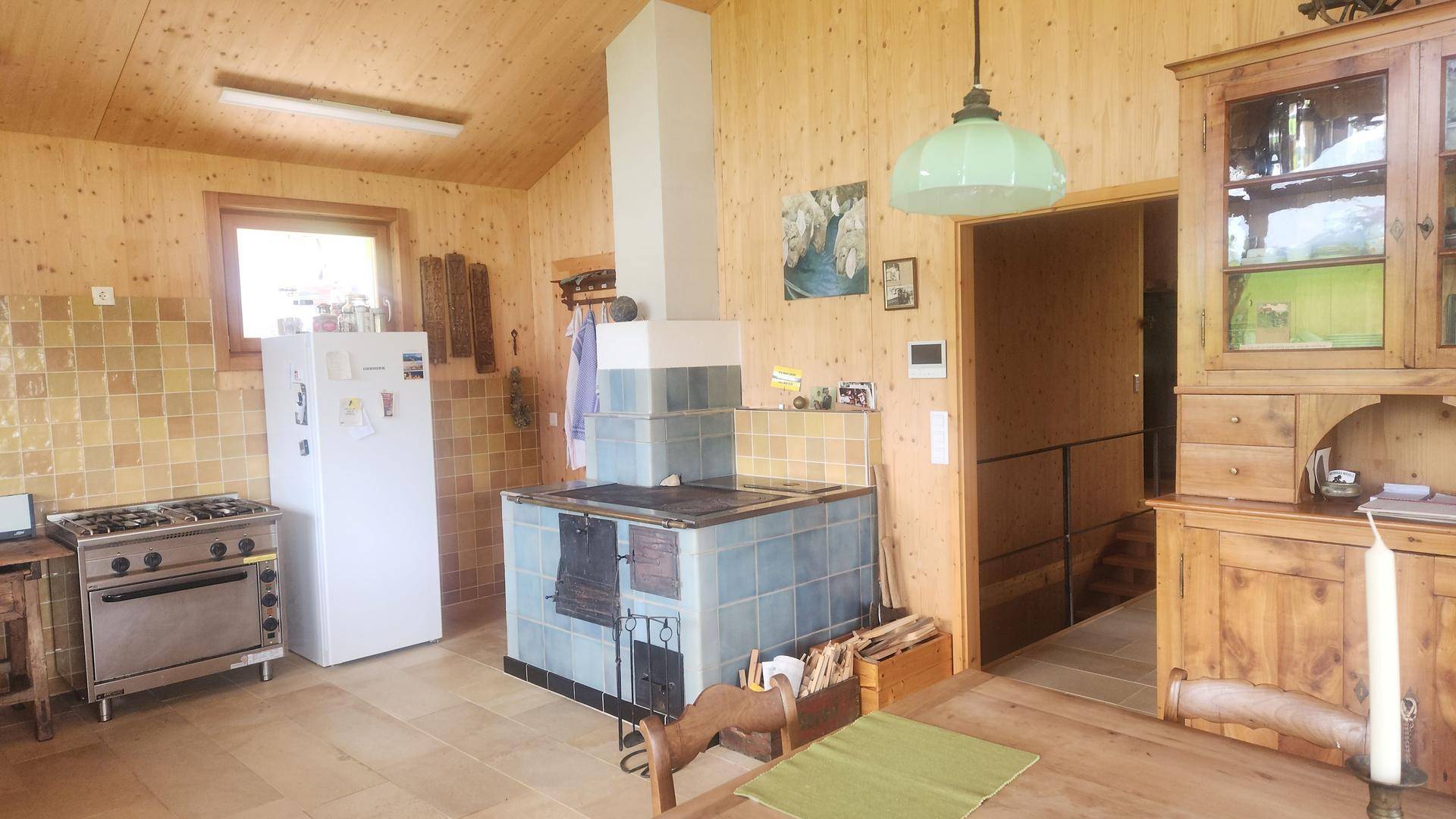 Rustikale Küche mit Holzwänden, traditionellem Kachelofen und Gasherd.