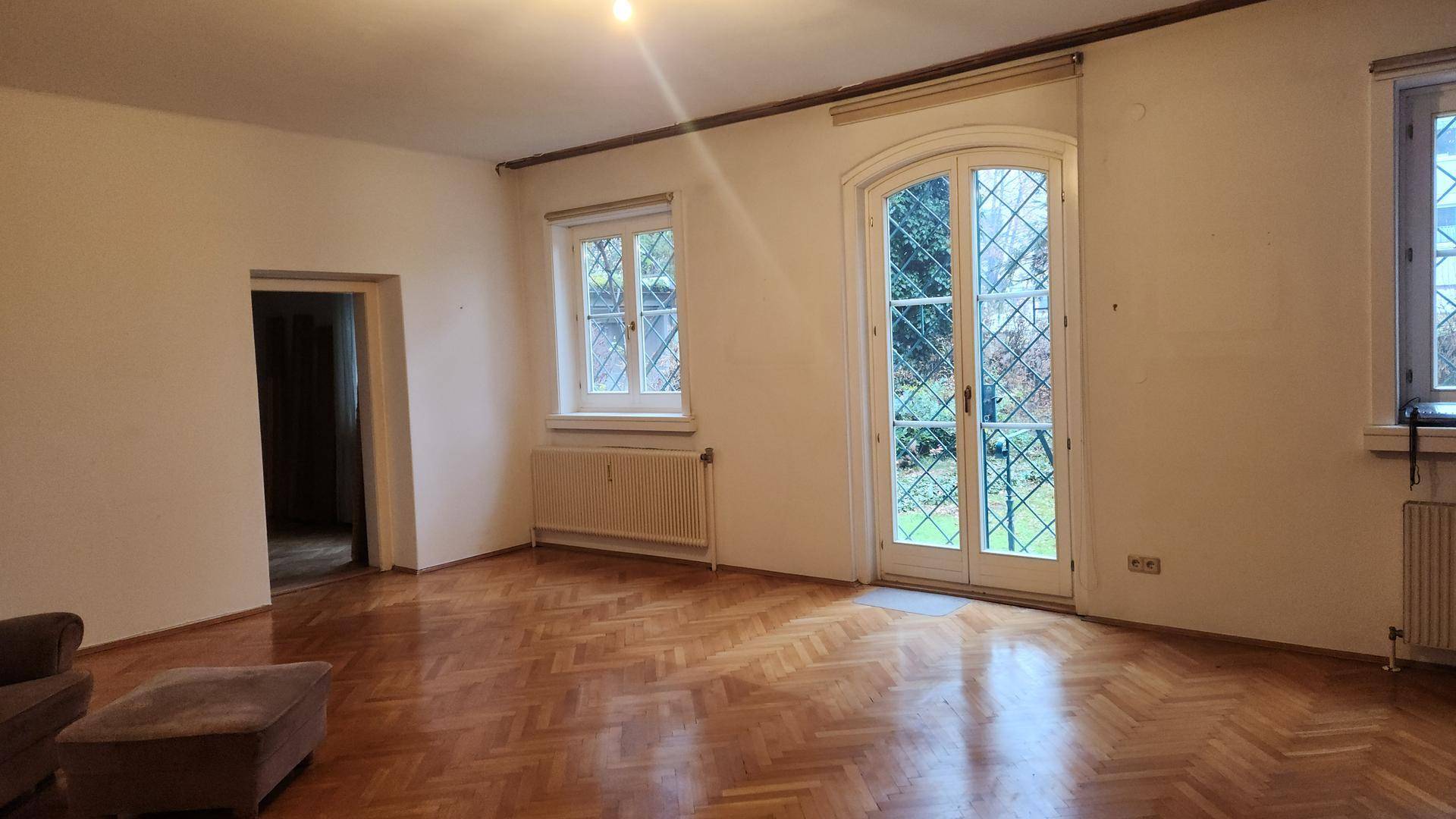 Heller Wohnraum mit Fischgrätparkett, großen Fenstern und direktem Zugang zum Gartenbereich.