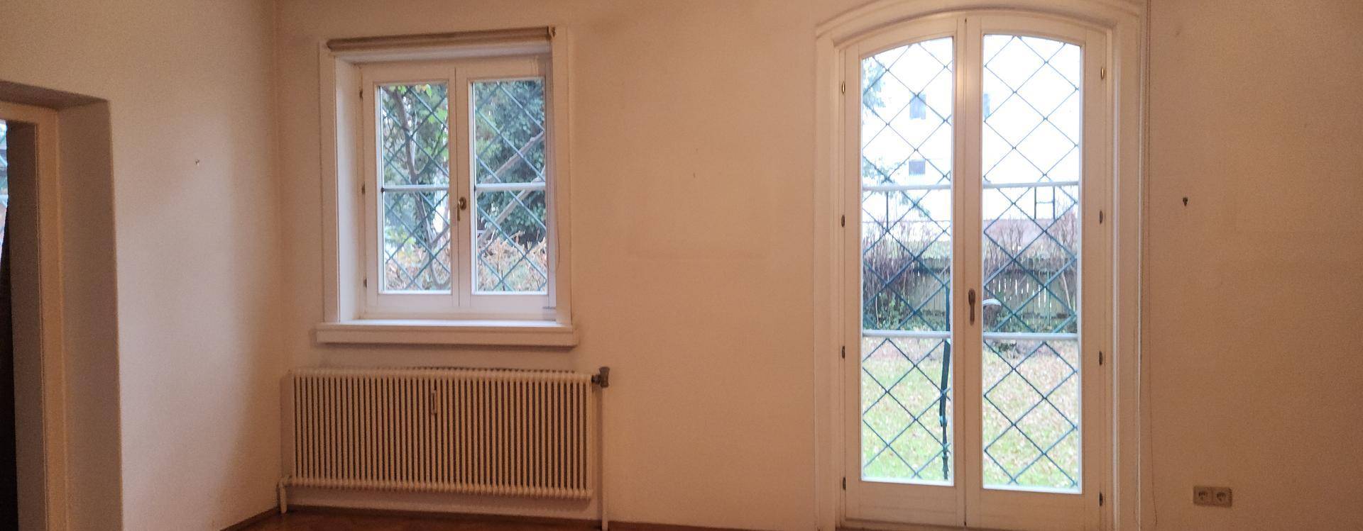 Detailansicht eines hellen Raumes mit Fischgrätparkett, Fenster und einer französischen Tür zum Außenbereich.