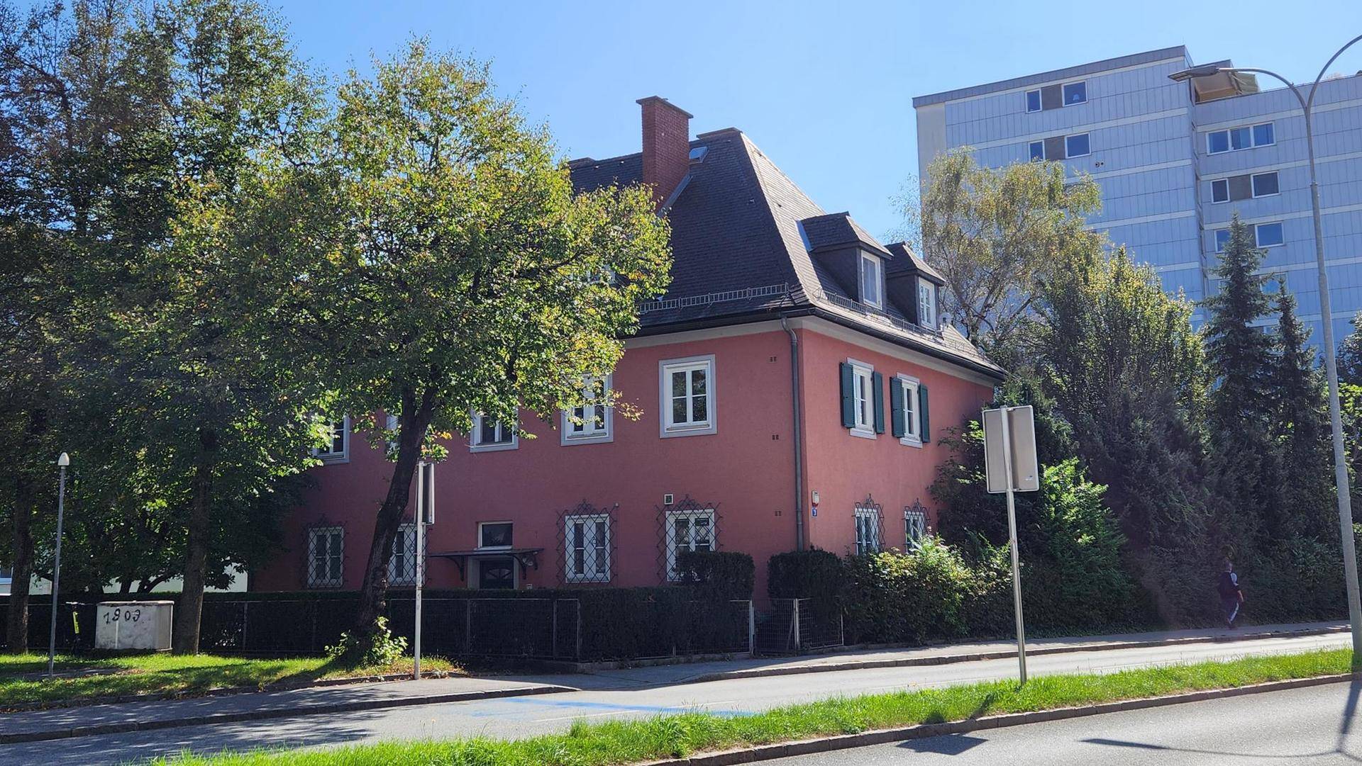 Gesamtansicht des historischen Hauses von der Straße mit gepflegter Hecke und Bäumen.