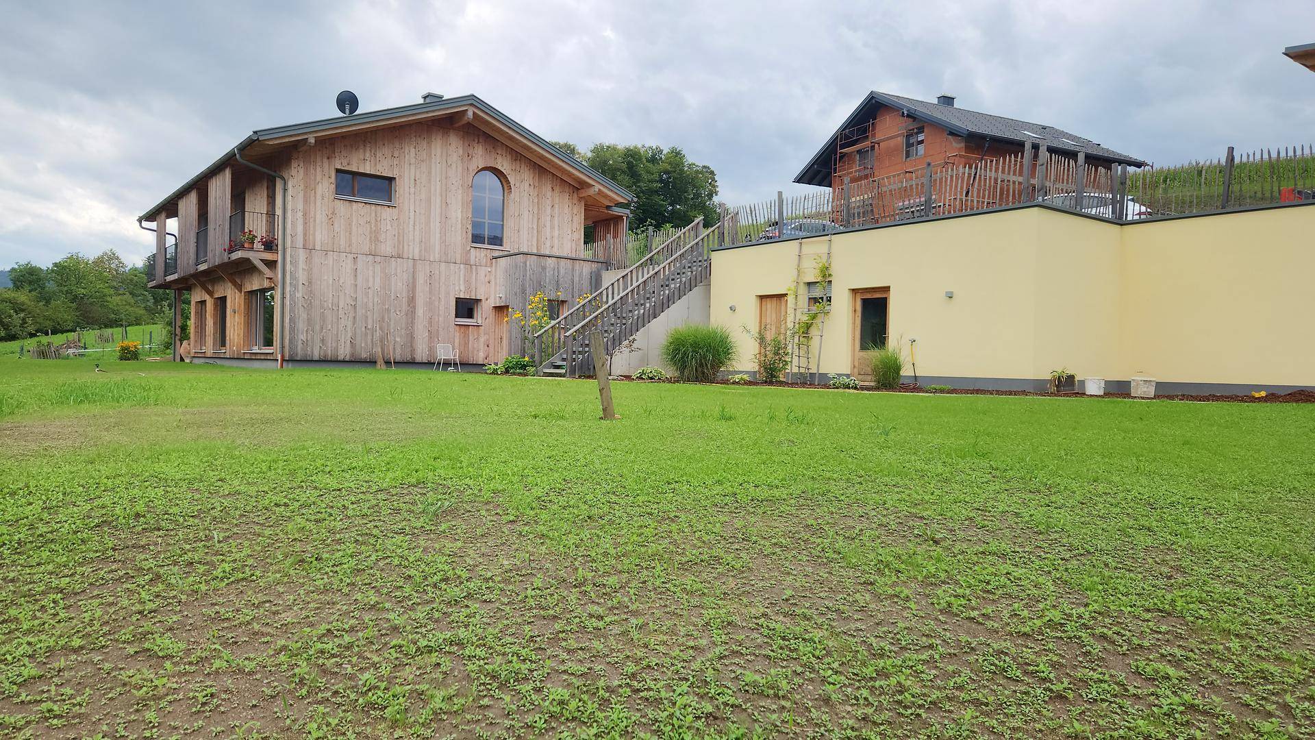 Großzügige Rasenfläche vor dem Holzhaus und einem angrenzenden Gebäude in ländlicher Umgebung.